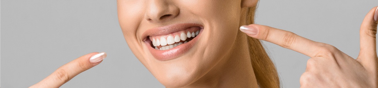 Close-up of a person smiling and pointing at their white teeth